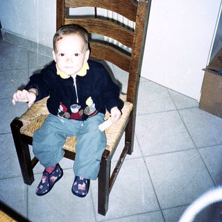 A young child sits on a chair in a room.