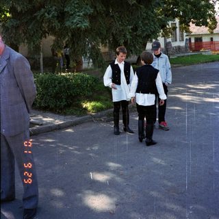 Three boys walk down a street, partially obscured by trees.