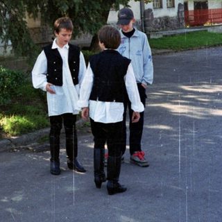 Three boys walk down a street, partially obscured by trees.