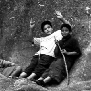 Three boys relax on a rock ledge outdoors.