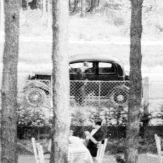 Black and white photo of tables, chairs, and people outdoors.