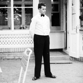 Man in formal wear stands outside a building.