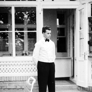Man in formal wear stands outside a building.