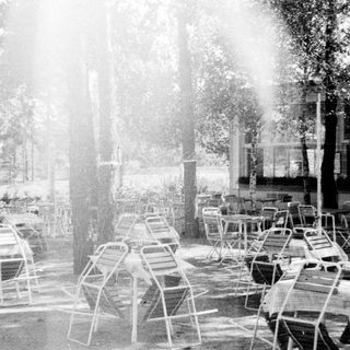 Monochrome image of a patio with tables and chairs.