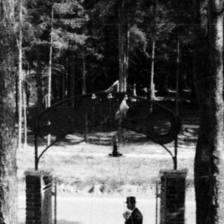 Man with stroller walks past outdoor tables and trees.
