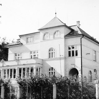 Black and white photo depicts a large, ornate house.