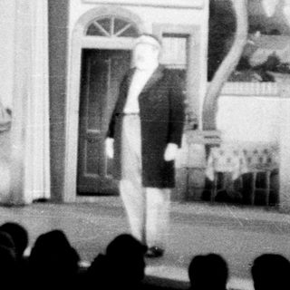 Stage set depicting a building with a performer on stage.