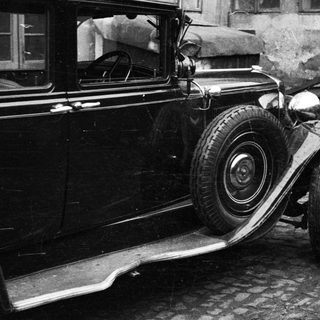 Vintage car parked next to a building and cart.