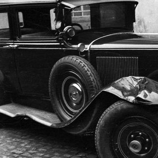 Black and white image of a vintage car near a building.