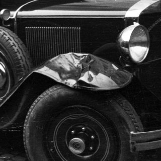 Black and white image of a vintage car near a building.