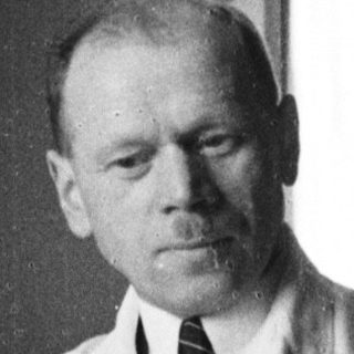 Man in lab coat seated at desk, light shining.