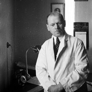 Man in lab coat seated at desk, light shining.