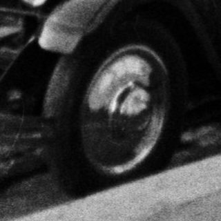Vintage car travels on a road with buildings in background.