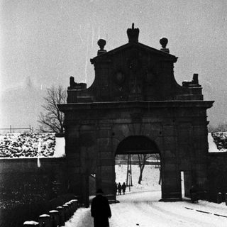 Man walks along snowy path through ornate gate.
