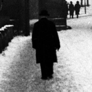 Man walks along snowy path through ornate gate.
