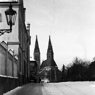 Snow-covered street leads to a church with twin towers.