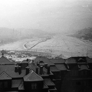 Snow-covered landscape with rooftops and industrial structures in the distance.