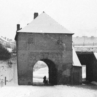 Snow-covered gatehouse and overpass with people walking by.