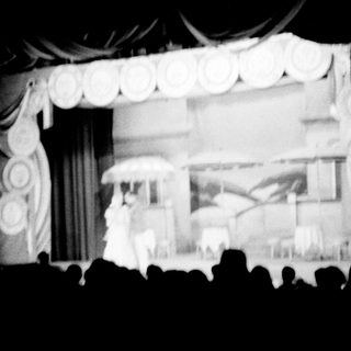 Stage performance with curtains, backdrop, and audience silhouettes.