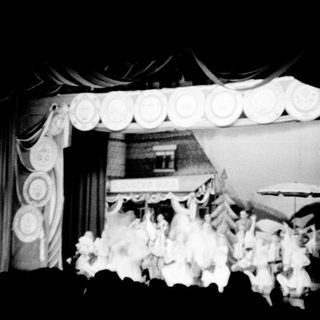 Black and white stage show with dancers and decorative backdrop.