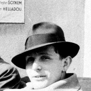 Two men in hats sit in an older car.