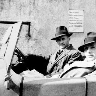 Two men in hats sit in an older car.