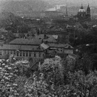 Monochrome cityscape, possibly Prague, with buildings and trees.