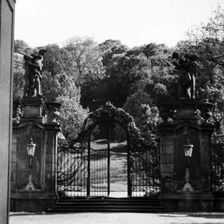 Ornate gate and statues overlook a formal garden landscape.