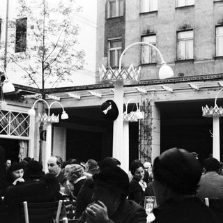Black and white photo of people seated under a porch.