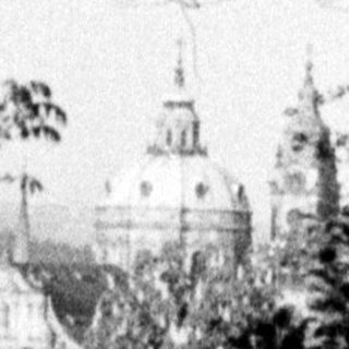 Here's a brief summary of the image: A building complex seen through trees and foliage.