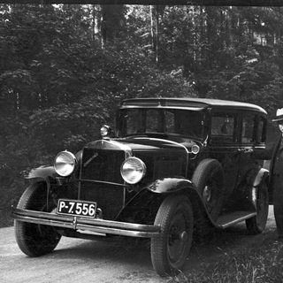 Man stands next to a vintage Chevrolet automobile on a road.