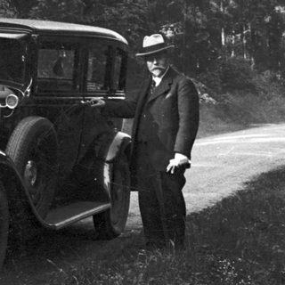 Man stands next to a vintage Chevrolet automobile on a road.