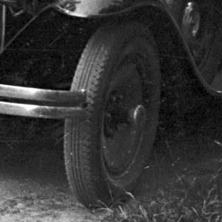 Man stands next to a vintage Chevrolet automobile on a road.