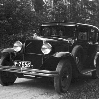 Vintage car and man standing on a dirt road.