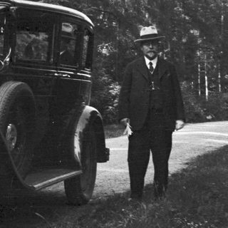 Vintage car and man standing on a dirt road.