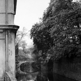 Still canal scene with wall, bridge, and trees.