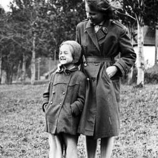 Here's a brief summary of the image: A woman and child stand in a grassy field.