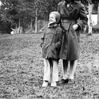 Here's a brief summary of the image: A woman and child stand in a grassy field.