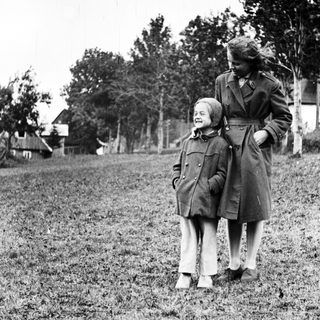 Here's a brief summary of the image: A woman and child stand in a grassy field.