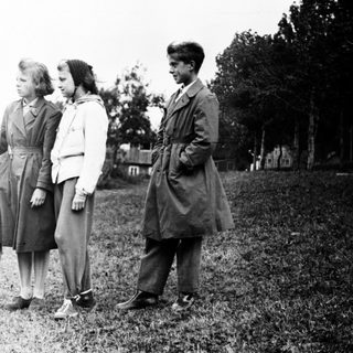 Four children stand outdoors on a grassy hillside.
