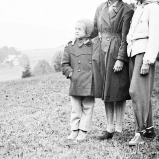 Four children stand outdoors on a grassy hillside.