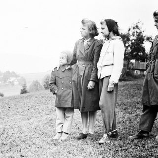 Four children stand outdoors on a grassy hillside.