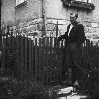 Man stands near a house with a picket fence.