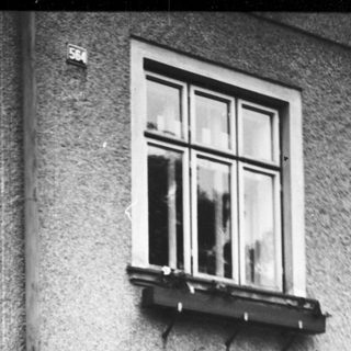 Man stands near a house with a picket fence.