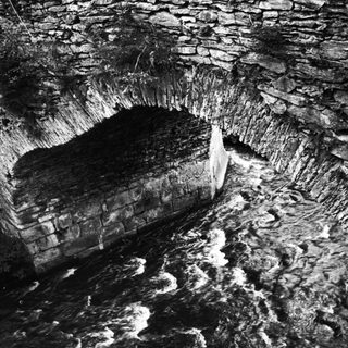 Arched stone structure above rushing water, viewed from above.