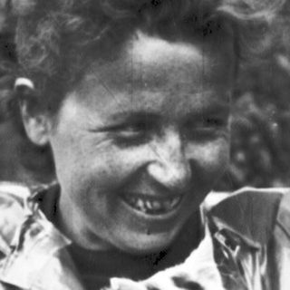 Woman in raincoat smiles, holding a small animal.