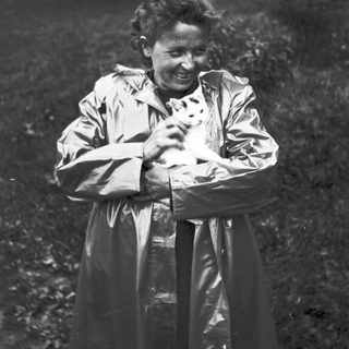 Woman in raincoat smiles, holding a small animal.