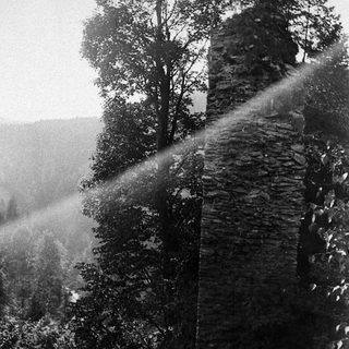 Ruined stone structure amidst trees, beams of light shining through.
