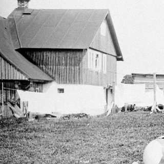 Here's a brief summary of the image: Group relaxing on grass near a barn and windmill.