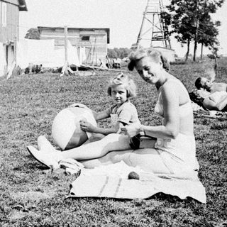 Here's a brief summary of the image: Group relaxing on grass near a barn and windmill.